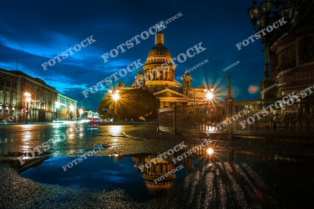 На фотографии запечатлен Исаакиевский собор в Санкт-Петербурге ночью. Подсветка и уличные фонари освещают грандиозное здание, подчеркивая его монументальность. Лужа на переднем плане отражает собор, создавая эффект двойного изображения. Этот исторический памятник, расположенный на Исаакиевской площади, является одним из символов города. Ночной вид собора добавляет загадочности и очарования.